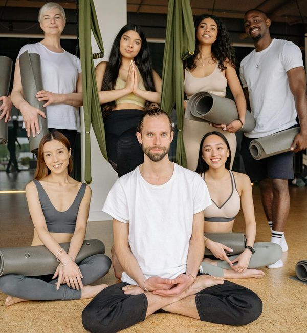 Diverse group of people smiling and stretching in a bright yoga class.