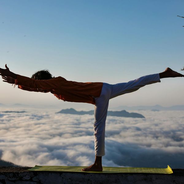 Silhouette of a person in a warrior yoga pose against a sunrise.